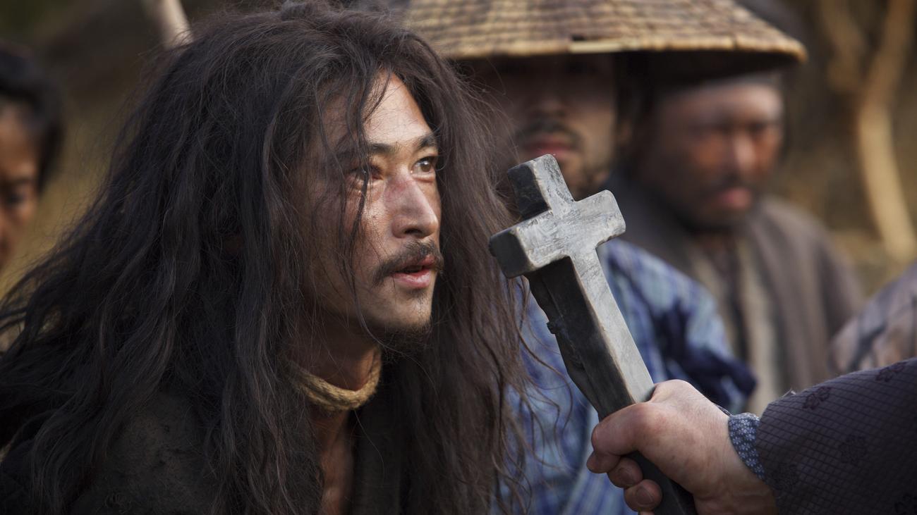 Kichijiro, a disheveled looking Japanese man with long hair and a moustache, with a cross being held in his face by a soldier, from the movie Silence.
Image copyright Paramount Pictures, 2016.